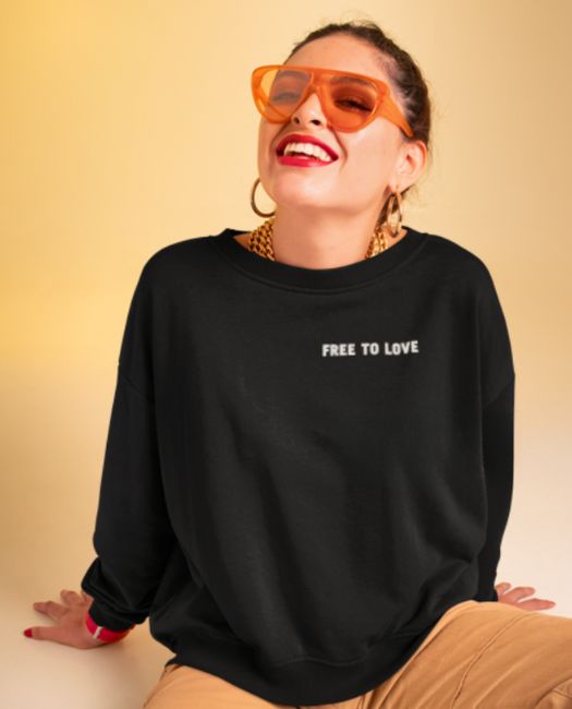 A smiling woman sitted on the floor wearing our 100% organic cotton black "free to love" sweathshirt